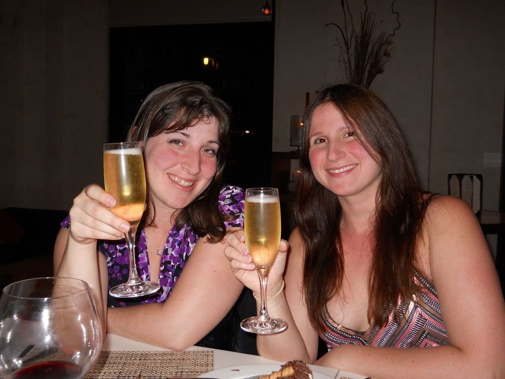 two women holding drinks and smiling at the camera