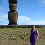 a woman posing in front of a large stone statue with Easter Island in the background