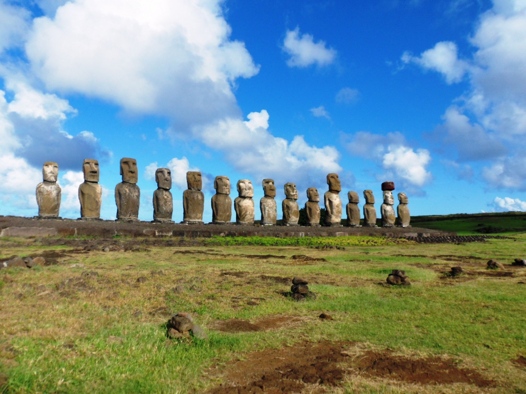 a row of stone statues in a grassy field with Easter Island in the background