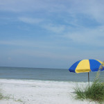 a beach with a blue and yellow umbrella
