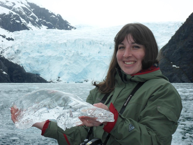 a woman holding an ice piece in front of a large glacier