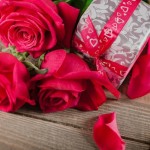 a gift box and roses on a wood surface