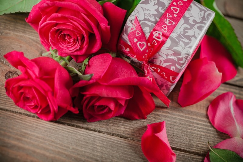 a gift box and roses on a wood surface