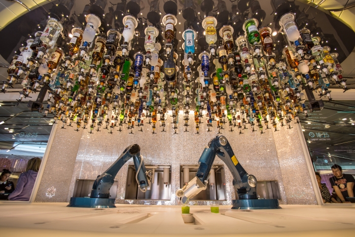 a group of robotic arms in a room with many bottles from the ceiling