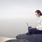 a woman sitting on a rock with a laptop