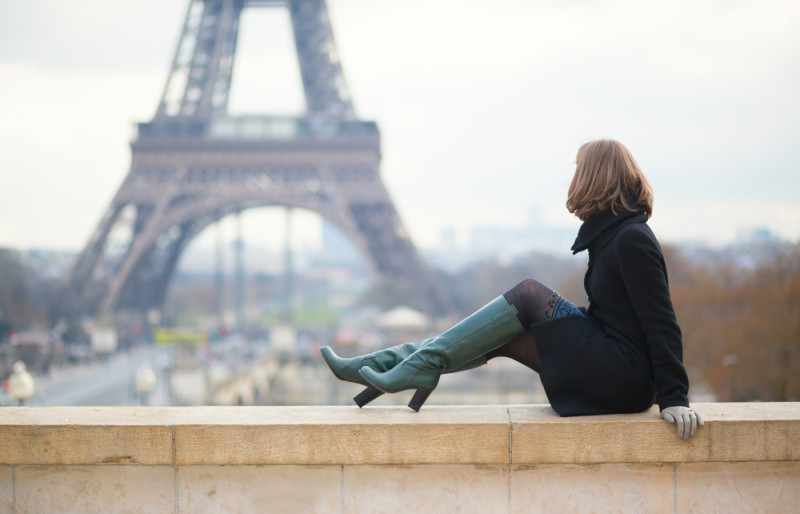 a woman sitting on a ledge with a tall green boots