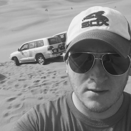 a man taking a selfie in the sand with a car in the background