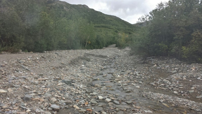 a rocky river bed with trees and hills in the background