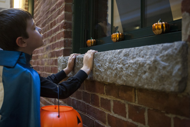 a boy in a cape holding a pumpkin on a ledge