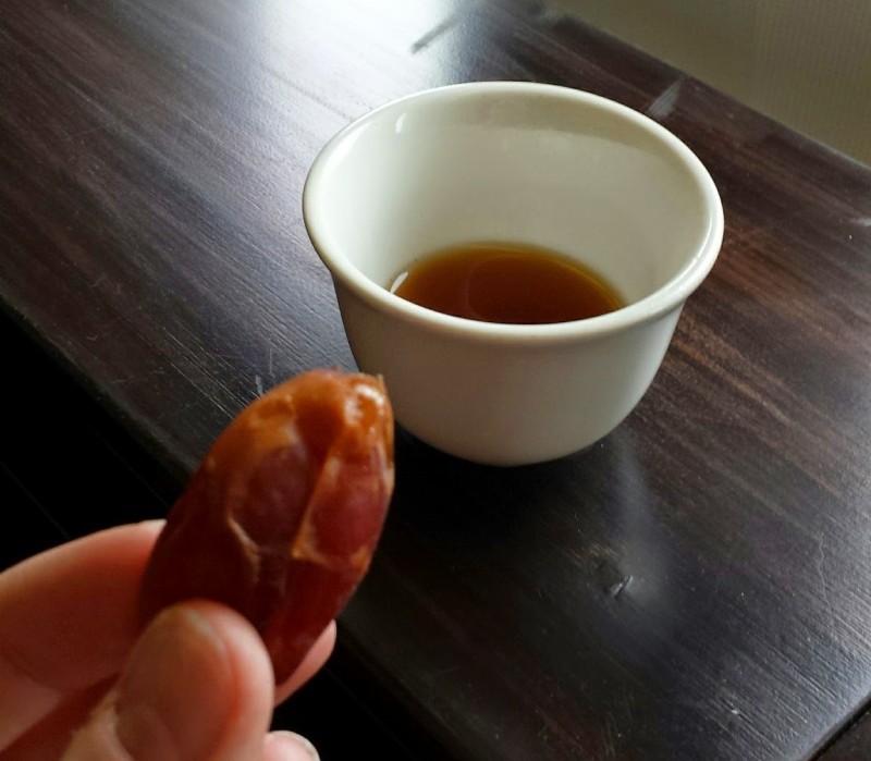 a hand holding a sausage next to a cup of tea
