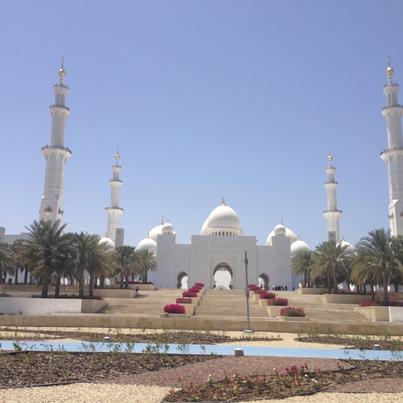 a white building with towers and a fountain with Sheikh Zayed Mosque in the background