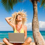a woman sitting on the beach with a laptop