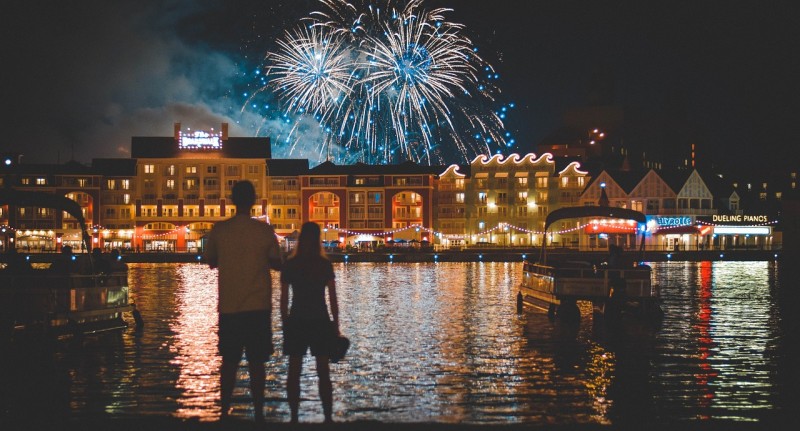a couple standing in front of a body of water with fireworks in the sky