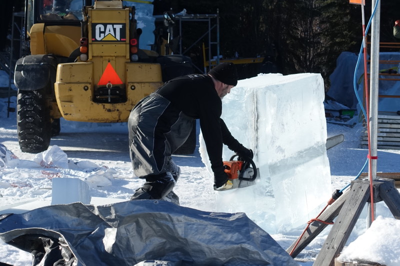 a man holding a chainsaw in front of a large block of ice