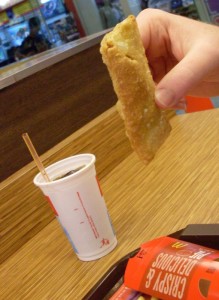 a hand holding a fried egg roll and a drink