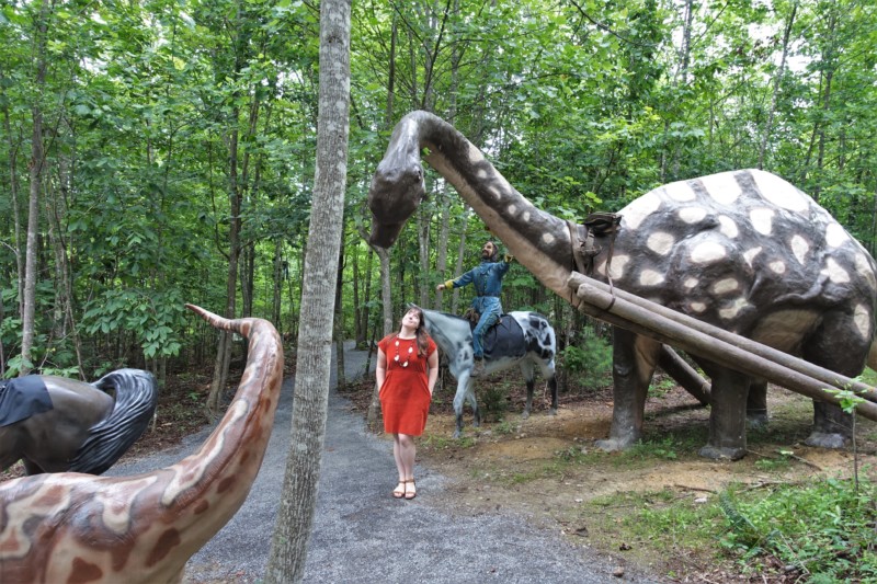 a woman standing in front of a statue of a dinosaur