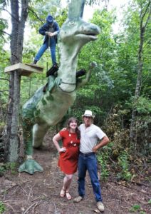 a group of people standing next to a statue of a dinosaur