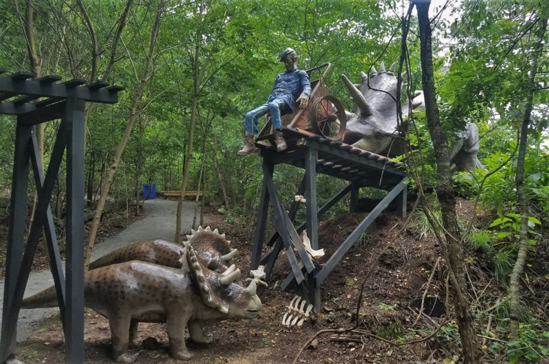 a statue of a man riding a cart on a platform with two dinosaurs