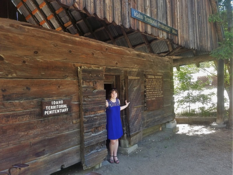 a woman in a blue dress standing in a doorway of a wooden building
