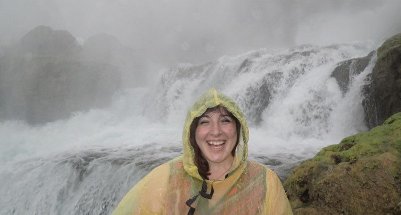 a woman wearing a raincoat in front of a waterfall
