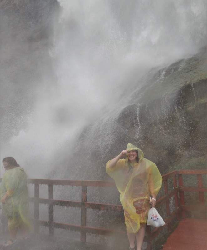 a woman in yellow raincoats standing on a railing in front of a waterfall