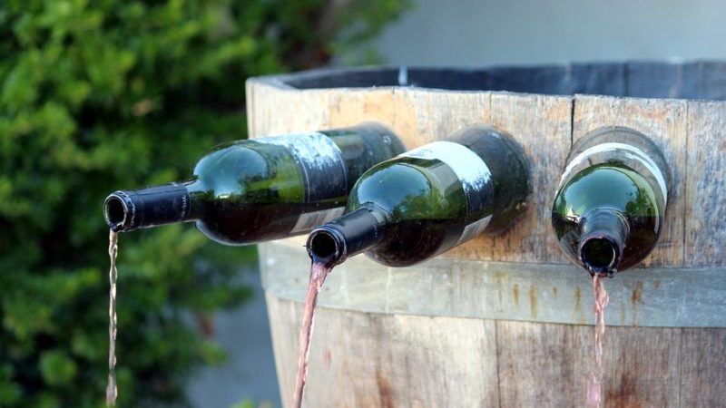 a wine bottle being poured into a barrel