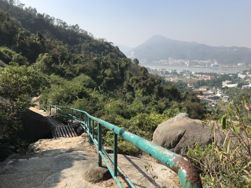 a green railing on a rocky path with trees and mountains in the background