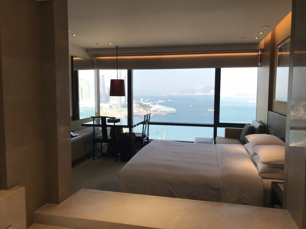 a room with a bed and a view of the water and city
